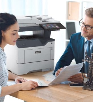 Ein Mann und eine Frau sitzen an einem Tisch und unterhalten sich, während in der Nähe ein Xerox®-Drucker steht. Ein Mann und eine Frau sitzen an einem Tisch und unterhalten sich, während in der Nähe ein Xerox®-Drucker steht.
