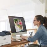 Eine Frau sitzt an einem Schreibtisch, konzentriert auf ihre Arbeit, mit einem Xerox® C320 Farbdrucker