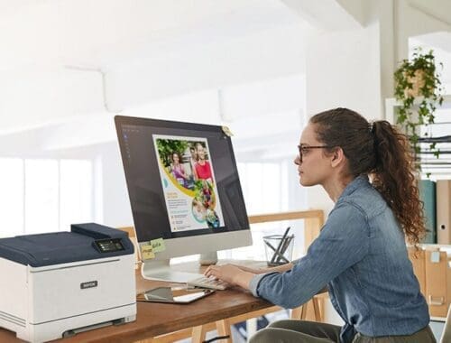 Eine Frau sitzt an einem Schreibtisch, konzentriert auf ihre Arbeit, mit einem Xerox® C320 Farbdrucker